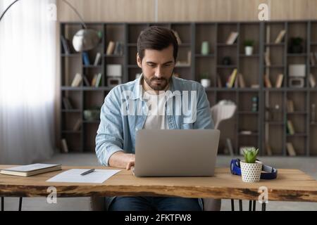 Confident businessman working on laptop online, sitting at wooden desk Stock Photo