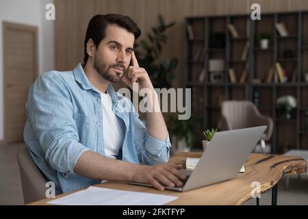 Pensive businessman looking to aside, pondering strategy, working on laptop Stock Photo