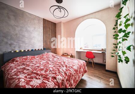 Interior design of light trendy bedroom in soft shade of red and deep gray colors. Comfortable bed, small nightstand and place for work in arched niche. Stock Photo