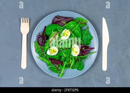 Quail eggs boiled on a lettuce leaf with microgreen sprouts with a wooden fork and spoon on a gray background. The concept of proper nutrition. Vegan Stock Photo