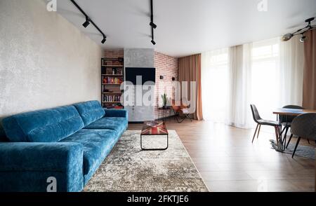 Fashionable modern design studio apartment with free layout in functional style. Blue sofa, coffee table, rack with books and others elements of decor creating cozy atmosphere recreation area. Stock Photo
