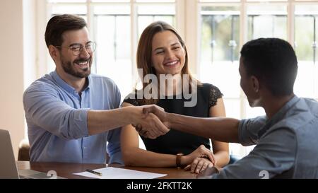 Happy millennial married couple shaking hands with financial advisor. Stock Photo