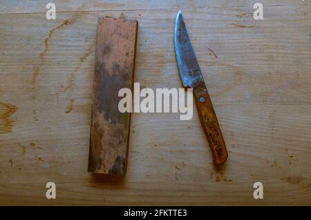 An old homemade knife and a whetstone. Sharpen a knife with a sharpening stone. Top. Stock Photo