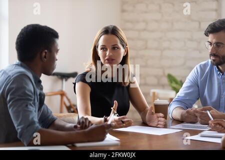 Serious young business lady discussing project with mixed race colleagues. Stock Photo