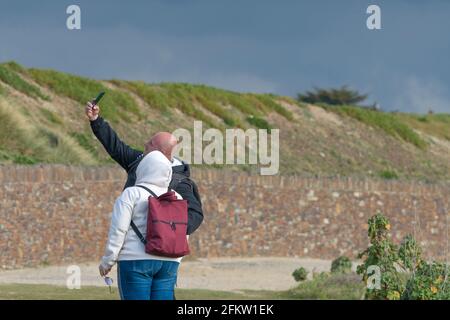 A couple of holidaymakers using a smartphone to take a selfie photograph on a staycation holiday in Newquay in Cornwall. Stock Photo