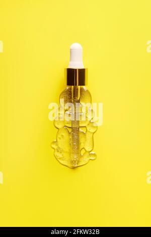 Liquid serum and dropper on a yellow background top view. Serum drops in the form of a bottle with a pipette. Stock Photo