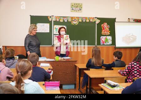 Chapaevsk, Samara region, Russia - January 23, 2021: Woman teacher in a mask stands in front of the class with a book in her hands Stock Photo