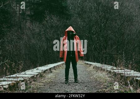 Man in orange hooded jacket with the gas mask on face on the old abandoned stone railway viaduct Stock Photo