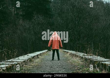 Man in orange hooded jacket with the mask in hand on the old abandoned stone railway viaduct. Stock Photo