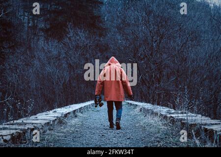 Man in orange hooded jacket with the mask in hand on the old abandoned stone railway viaduct. Stock Photo