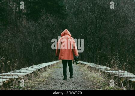 Man in orange hooded jacket with the mask in hand on the old abandoned stone railway viaduct. Stock Photo
