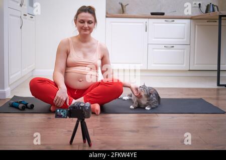 A pregnant woman is engaged in fitness in the home kitchen and conducts classes online through the camera Stock Photo