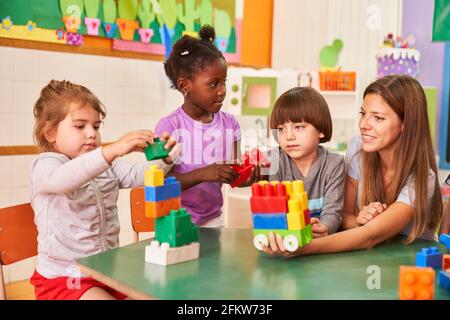 Childminder and children in international kindergarten play with building blocks Stock Photo