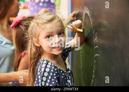 Little girl in preschool or kindergarten while painting with chalk on the blackboard Stock Photo