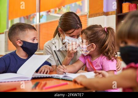 Kindergarten teacher or childminder helps children learn with face masks because of Covid-19 Stock Photo