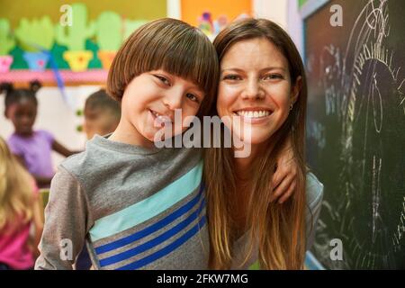 Happy boy with teacher or childminder in front of a blackboard in a preschool or daycare center Stock Photo