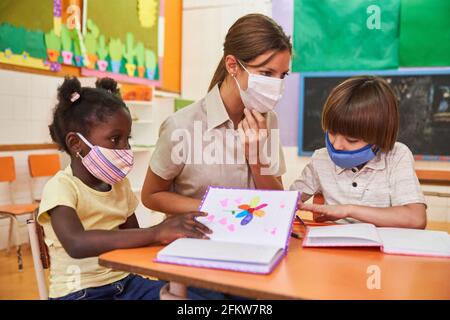 Childminder and children with face masks because of Covid-19 in kindergarten study together Stock Photo