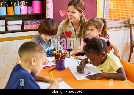 Childminder and multicultural children painting with crayons in the international after-school care center Stock Photo