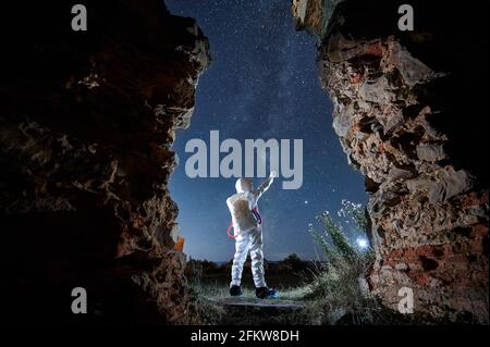Back view of spaceman in white suit and helmet standing and exploring beautiful starry sky at night. Concept of cosmic traveler. Stock Photo
