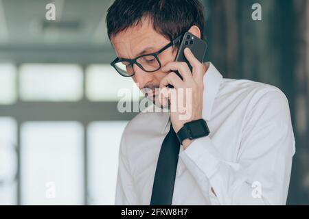 Serious businessman talking on mobile phone in the office, selective focus portrait Stock Photo
