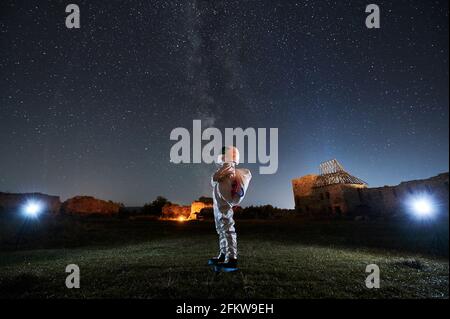 Spaceman in special space suit and helmet standing and looking on starry sky with Milky way at night. Stock Photo