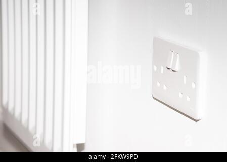 A United Kingdom standard wall socket on a white wall next to radiator Stock Photo
