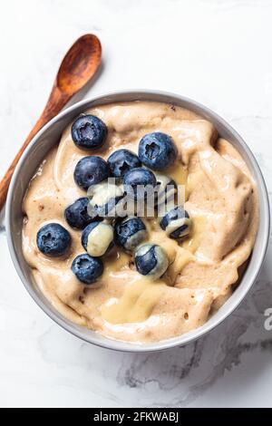 Banana dairy-free ice cream or vegan smoothie bowl with berries and peanut butter, white marble table.