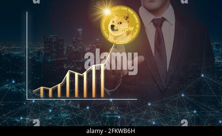 Businessman on a night city background pointing finger at virtual digital gold dogecoin and positive growth arrow. Business development, investment an Stock Photo