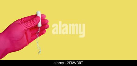 Woman wearing pink glove and holding a cotton tampon against yellow background. Stock Photo