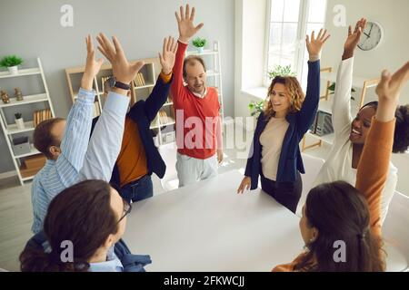 Diverse multiracial different age team standing around table with raised hand Stock Photo