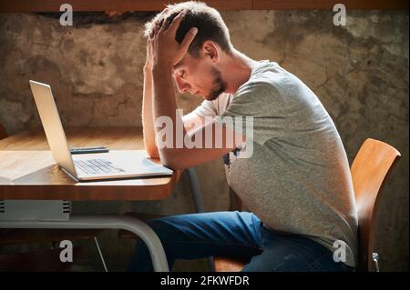 Side view of irritated and pensive young man working or studying in laptop. Concept of thinking about working in home. Stock Photo
