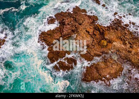 Aerial view of blue ocean washing around the surrounding etched rocks and boulders Stock Photo