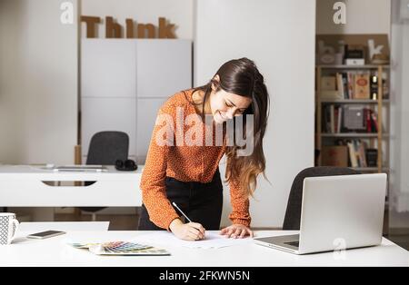 Young businesswoman standing in her home office and writing notes - business concept Stock Photo