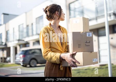 Woman holding parcels on the street in front of the house. Received the ordered goods at the post office. Online shopping. Delivery service.  Stock Photo
