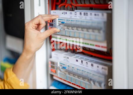 Close up on woman hand turn on the machine on the electrical panel at house.  Stock Photo