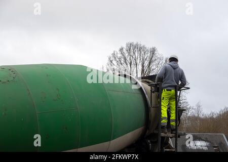 Man worker on a ladder checking concrete mixer truck. Construction worker in housing development. Stock Photo
