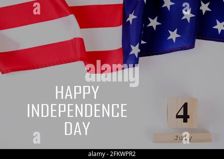 Ruffled American flag and wooden cube calendar with 4th of July congratulations. Happy Independence Day greeting card text on grey copy space backgrou Stock Photo