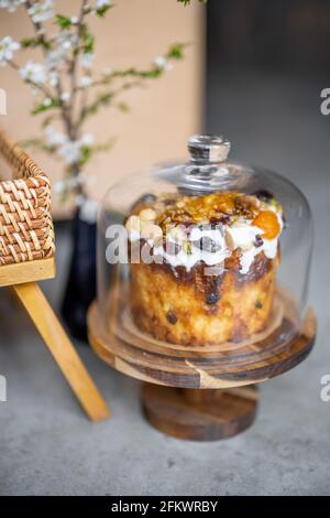 Delicious Easter sweet cupcake decorated with dried fruits and nuts on cake stands with glass cloche and spring branch with white flowers in vase. Stock Photo