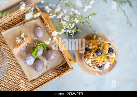 Delicious Easter sweet cupcake decorated with dried fruits and nuts on wooden cake stands and spring branch with white flowers in vase and naturally painted eggs. Top view. Stock Photo
