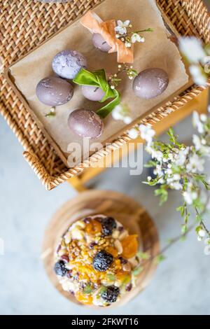 Delicious Easter sweet cupcake decorated with dried fruits and nuts on wooden cake stands and spring branch with white flowers in vase and naturally painted eggs. Top view. Stock Photo