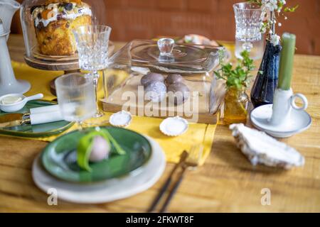 Happy Easter concept. Beautiful spring table settings, green plate with egg, panettone on cake stand, green candles, and branch of apple flowers in vase. Holiday tablescape.  Stock Photo