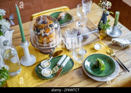 Happy Easter concept. Beautiful spring table settings, green plate with egg, panettone on cake stand, green candles, and branch of apple flowers in vase. Holiday tablescape.  Stock Photo