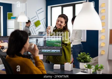 Videographers drinking coffee and talking during work break sitting at desk in creative agency office. Video editor and sound engineer working at project, editing film footage in software app Stock Photo