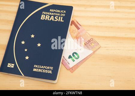 Brazilian passport with a 10 euro note on the side, on a wooden table. Stock Photo