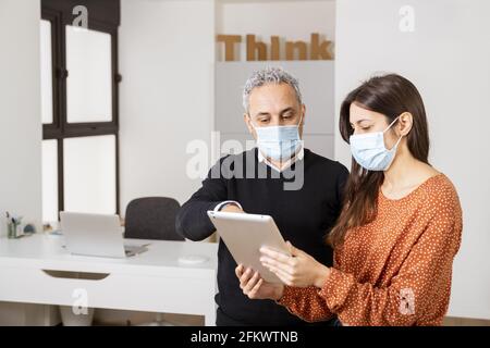 Workers in masks discussing the project using a tablet - business concept Stock Photo