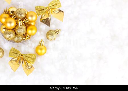 Bright golden and yellow Christmas decorations (ribbons, baubles, ornament) flat lay on white artificial snow background with copy space. Christmas an Stock Photo