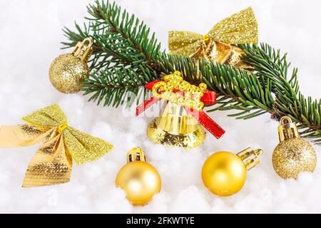 Bright golden and yellow Christmas decorations (ribbons, baubles, ornaments, bell) with fir tree branch on white artificial snow background. Christmas Stock Photo