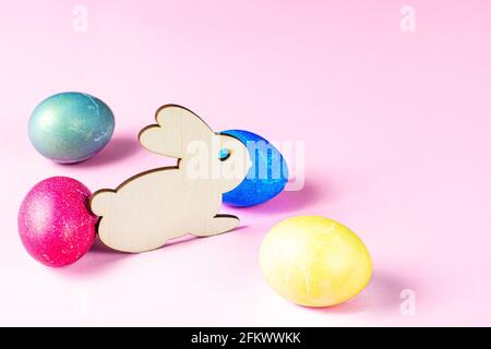 Funny wooden Easter Bunny with colorful eggs as symbols of a holiday with copy space on light pink background. Stock Photo