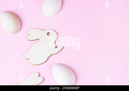 Top view of funny wooden Easter Bunny with eggs as symbols of a holiday with copy space on light pink background. Stock Photo