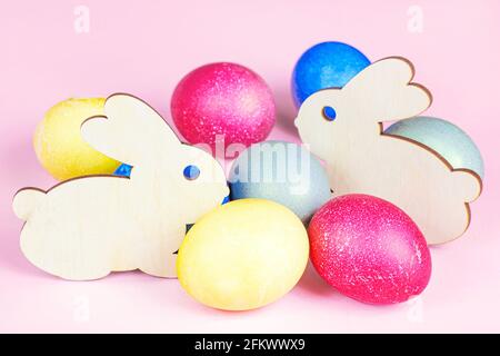 Funny wooden Easter Bunny with colorful eggs as symbols of a holiday on light pink background. Stock Photo
